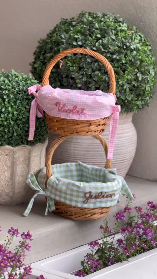 Two small wicker baskets with gingham fabric liners and embroidered names outdoors.