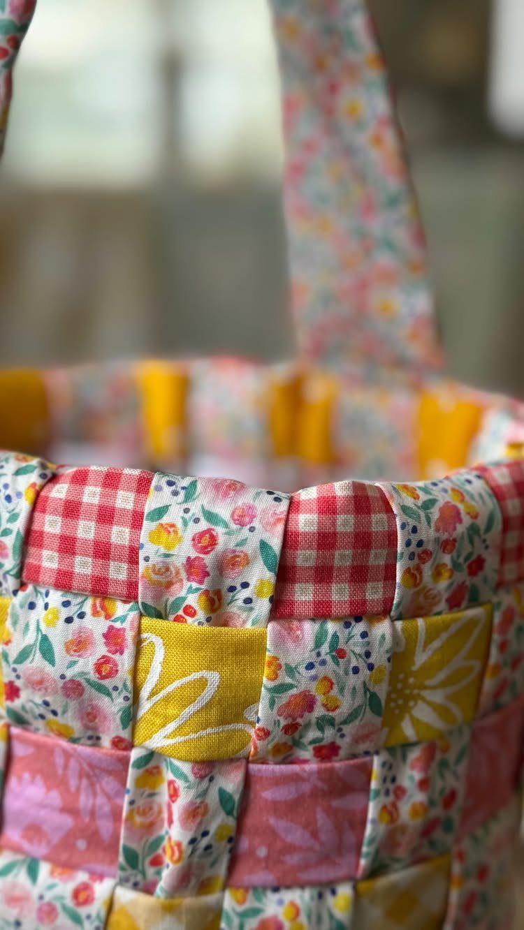 Small woven fabric basket with colorful floral and gingham patterns and a handle.