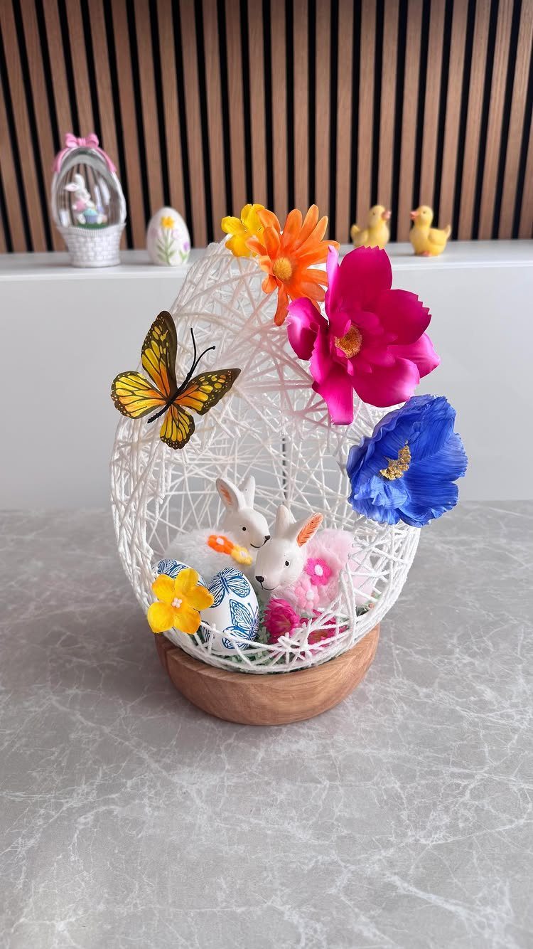 White woven egg basket with bunny figurines, colorful flowers, and a yellow butterfly.