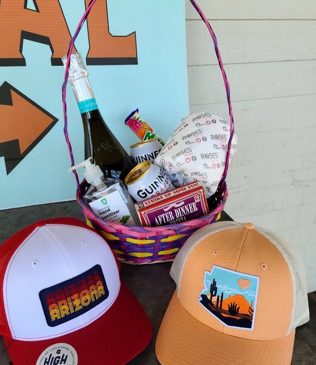 Gift basket with beer, wine, and chocolates next to two baseball caps.