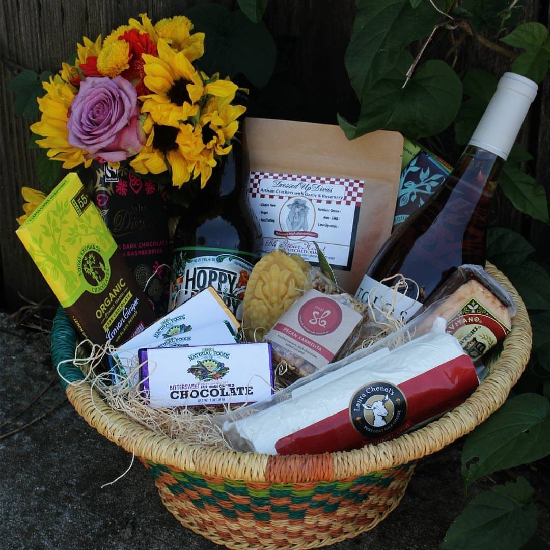Woven gift basket filled with wine, cheese, and chocolate next to sunflowers.