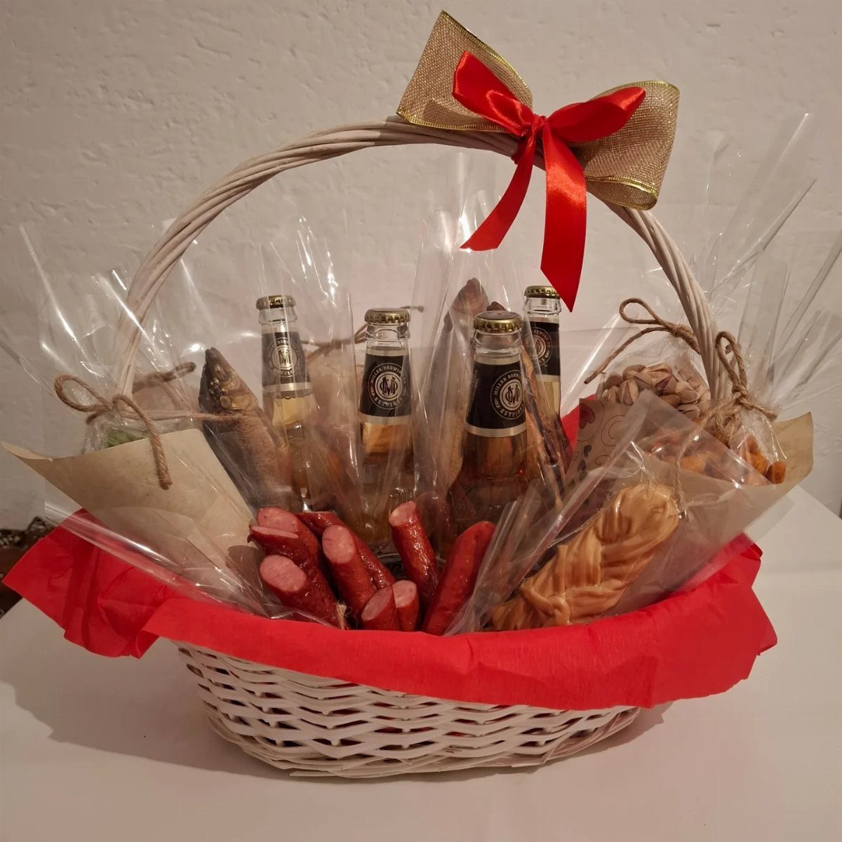 White wicker gift basket filled with beer bottles, sausages, and snacks wrapped in cellophane.