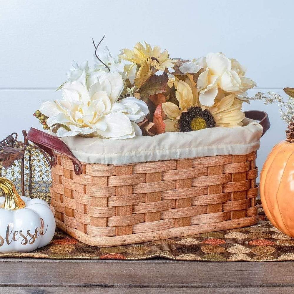 Woven wicker basket filled with autumn flowers next to white and orange pumpkins.