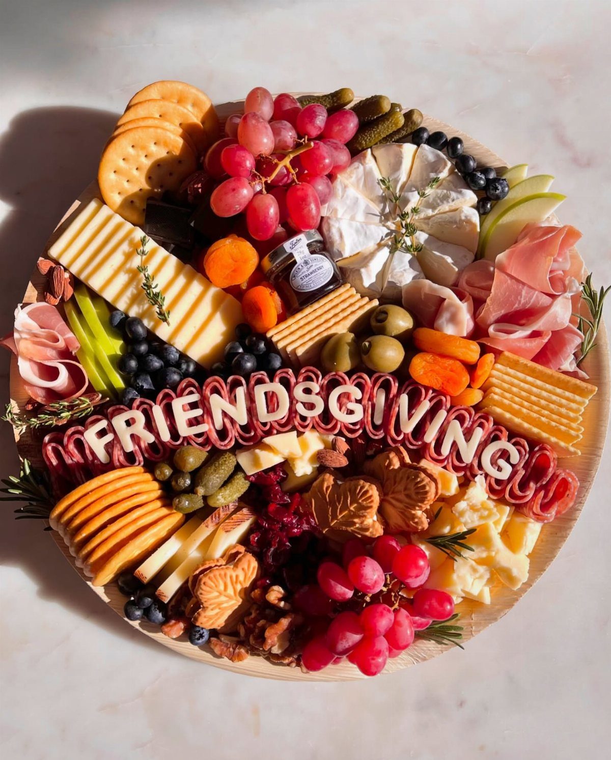 Charcuterie board with meats, cheeses, and fruits spelling out Friendsgiving in the center.