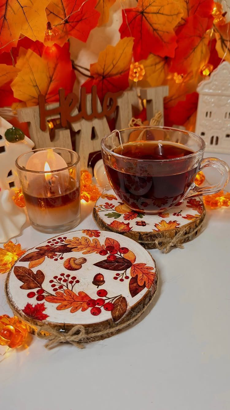 Wood slice coasters with autumn leaf patterns holding a cup of tea and candle.