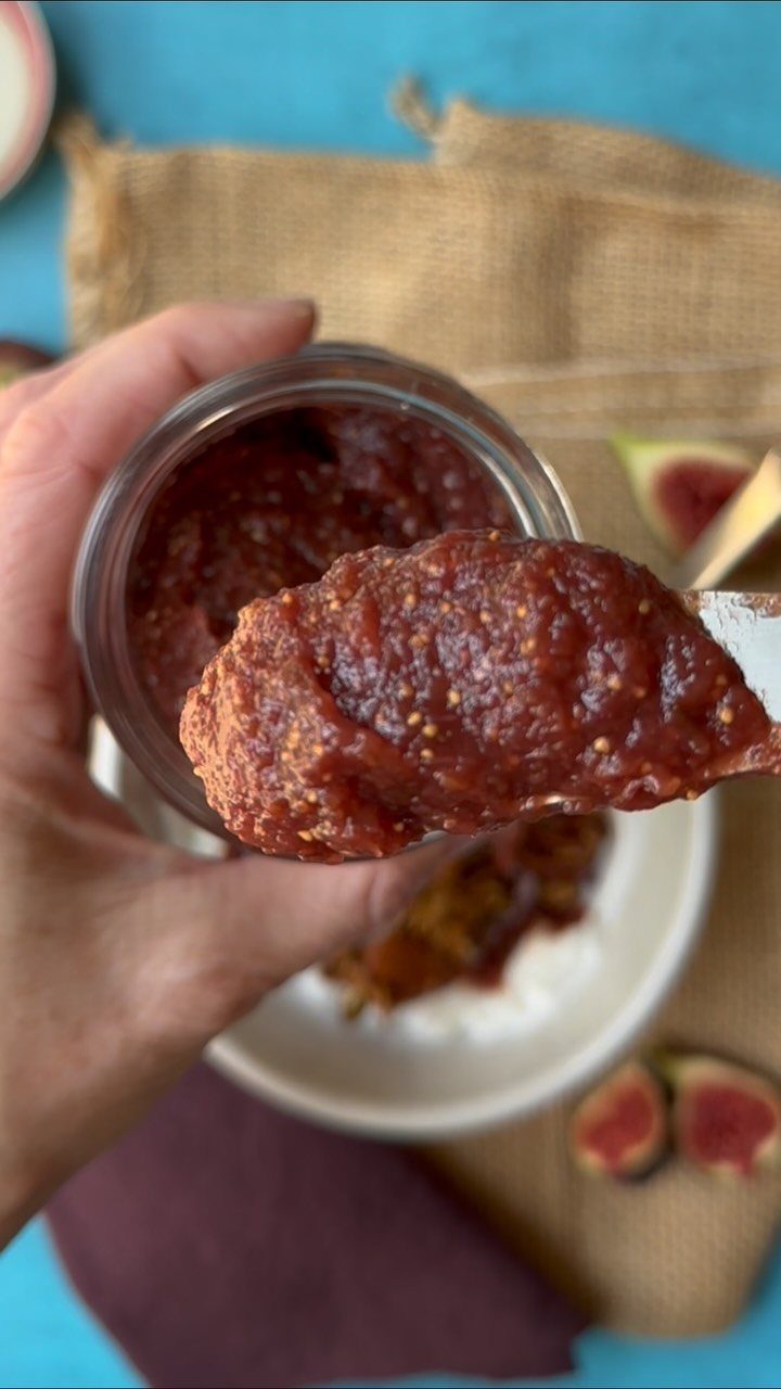 Reddish-brown fig jam in a glass jar with a spoonful lifted up.
