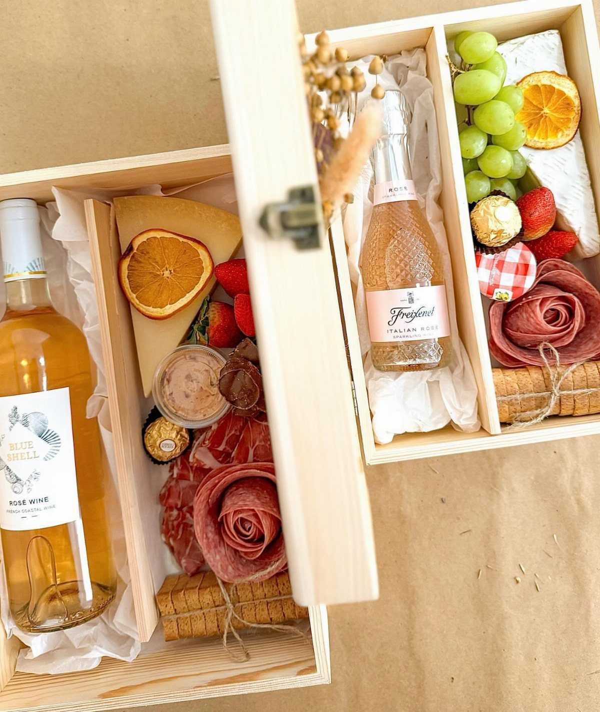 Two wooden gift boxes filled with charcuterie, wine, cheese, and fresh fruit.