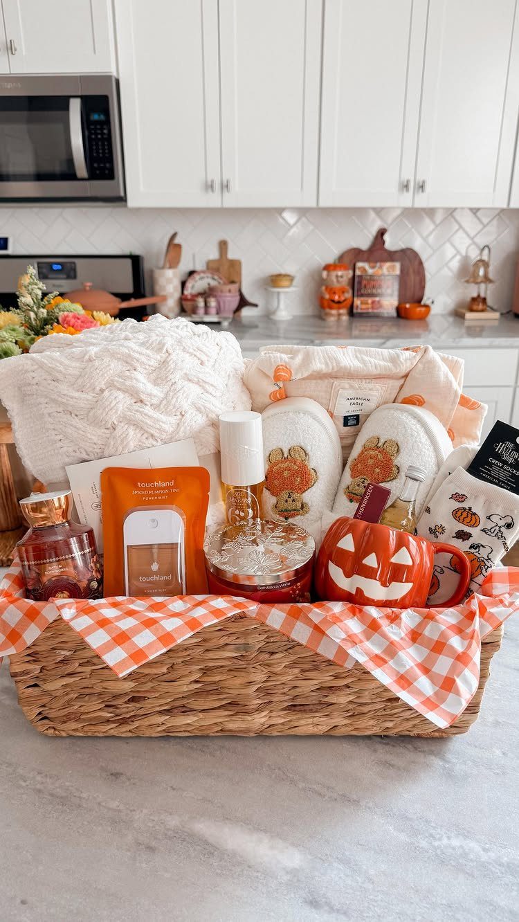 Autumn gift basket with pumpkin mug, slippers, and white blanket on marble counter