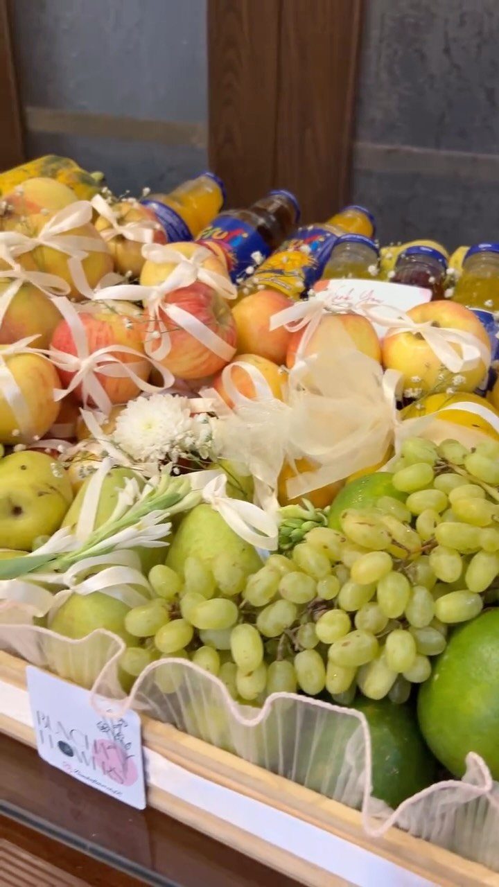 Fruit basket with green grapes, apples, pears, and juice bottles in wooden crate