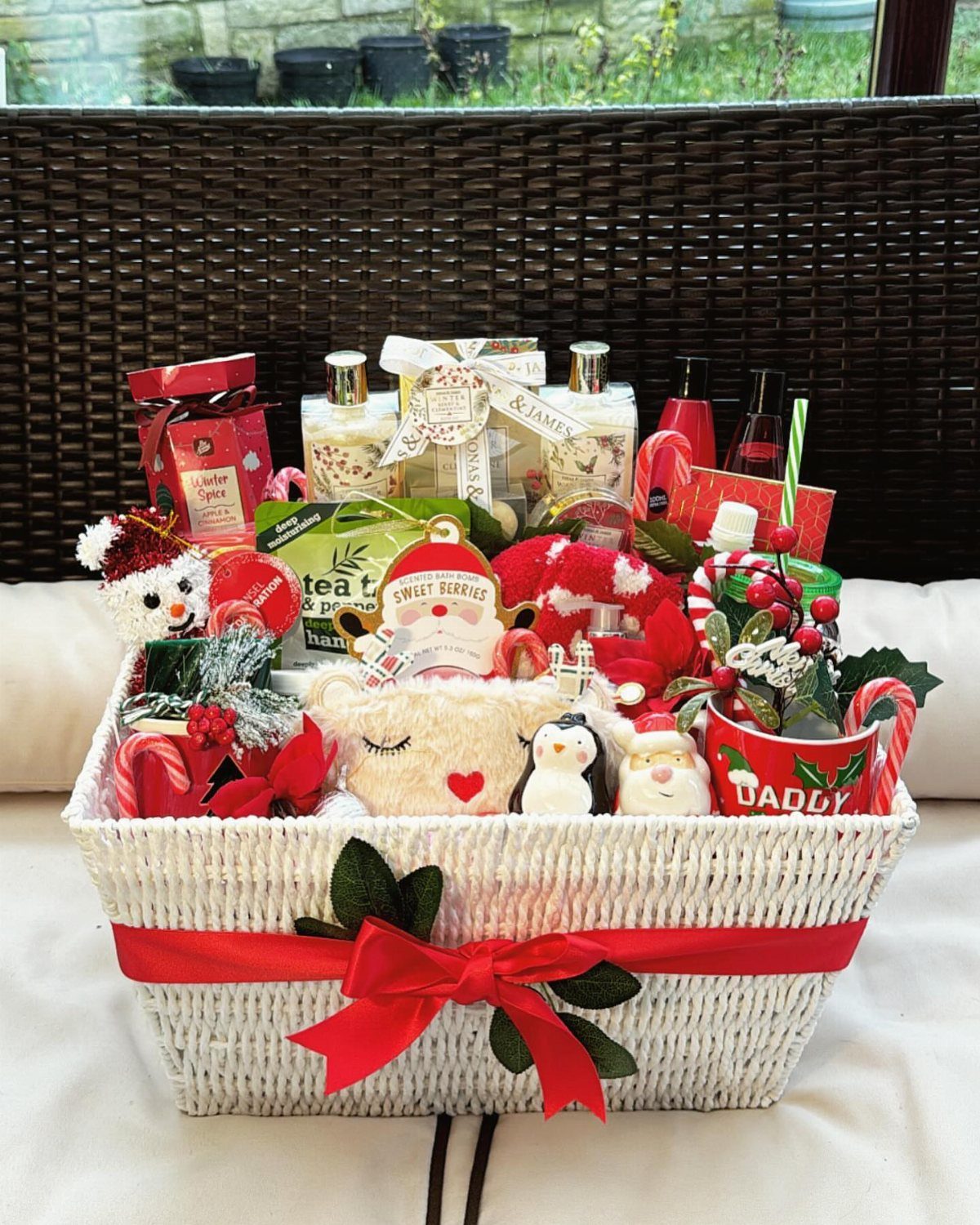 White wicker gift basket with red ribbon filled with Christmas plushies and treats.