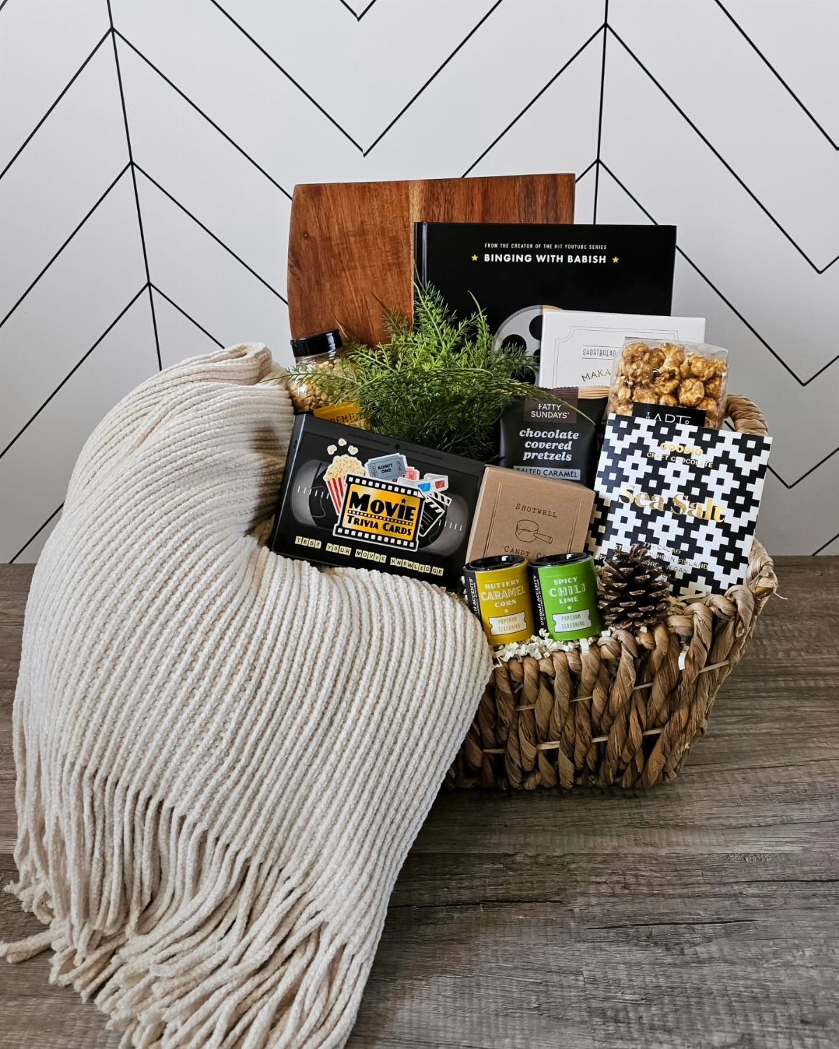 Woven gift basket with movie snacks, a throw blanket, and a black book.