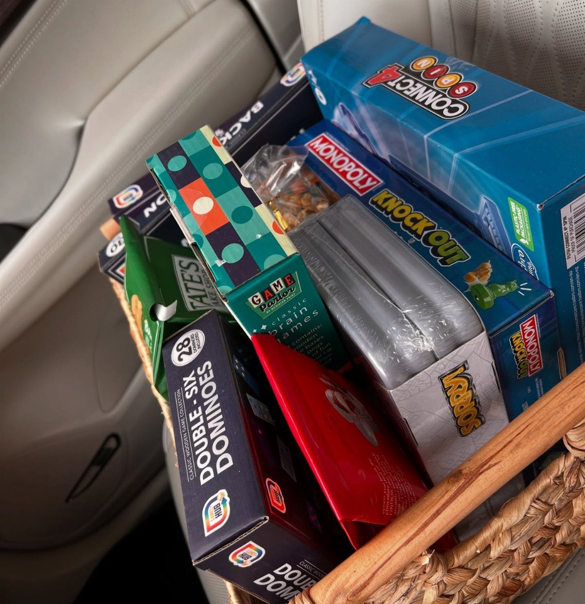 Woven basket filled with board games and snacks on a white car seat.
