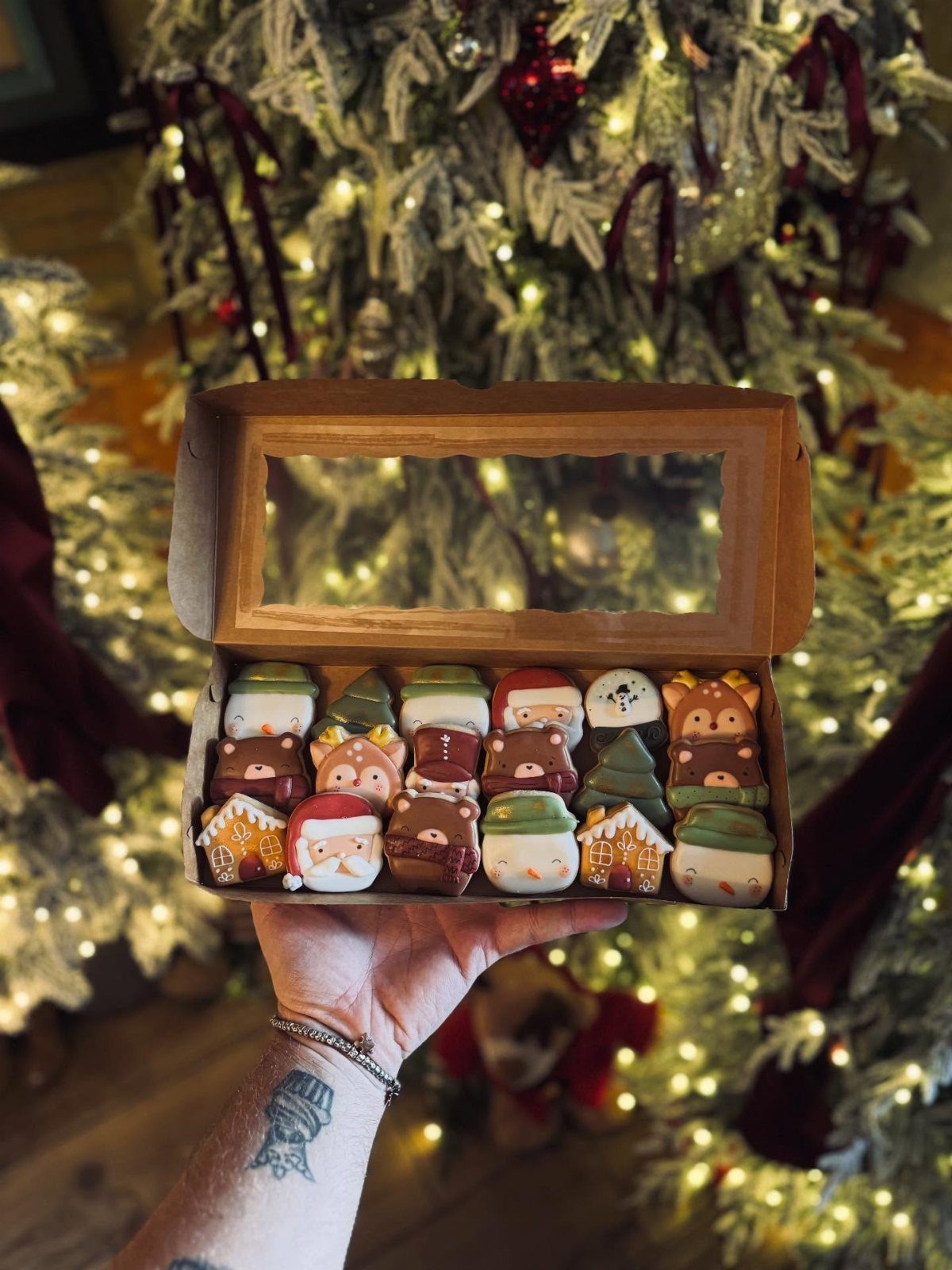 Decorated Christmas cookies in a cardboard box held in front of a lit tree