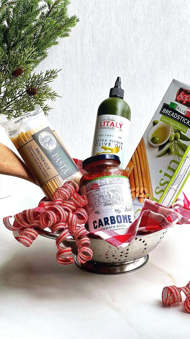 Pasta, tomato sauce, olive oil, and breadsticks arranged in a metal colander gift basket.