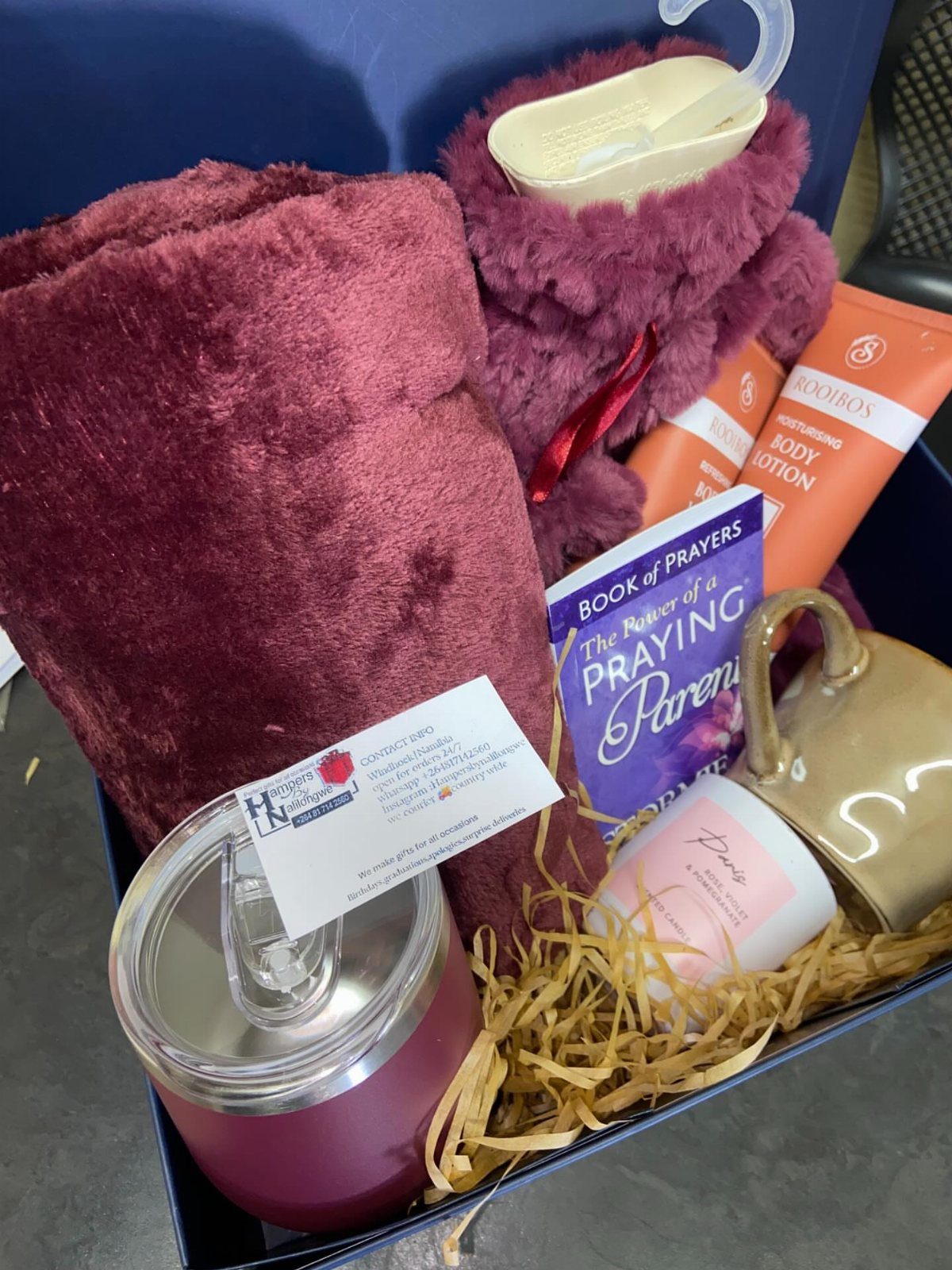 Relaxation gift basket with burgundy blanket, purple slippers, candle, and body lotion.