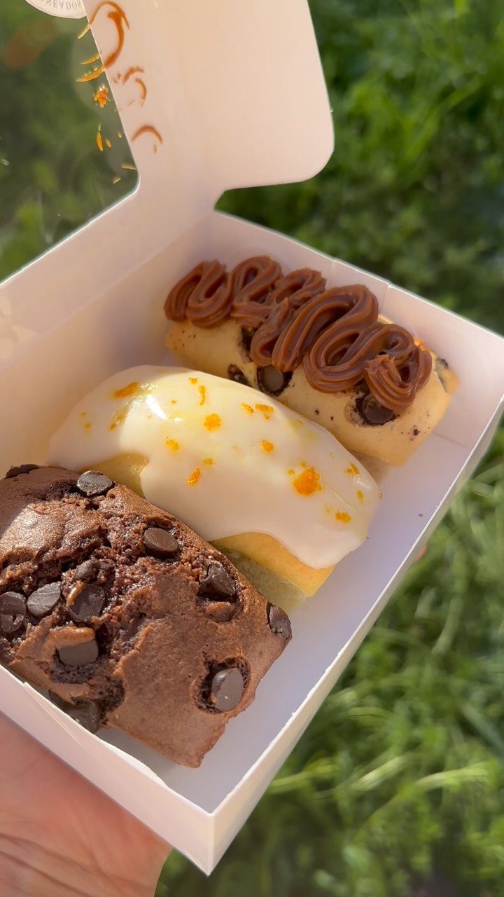 Three small frosted baked loaves in a white gift box over green grass.