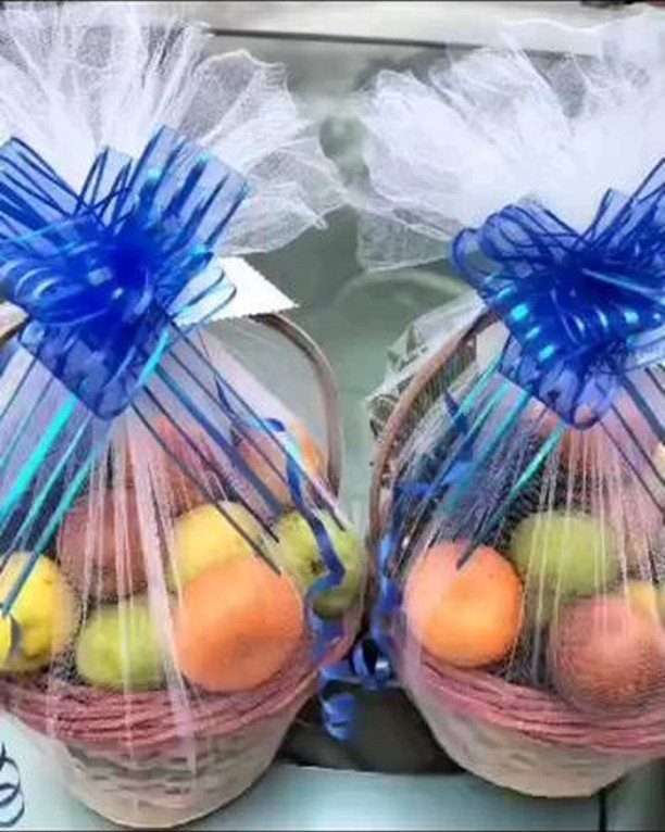 Two fruit gift baskets wrapped in cellophane with large blue ribbons.