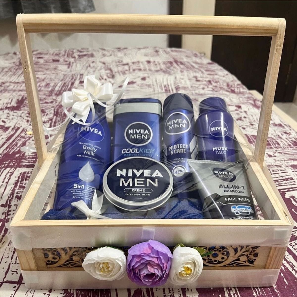 Wooden gift basket filled with blue Nivea Men grooming products and artificial flowers.