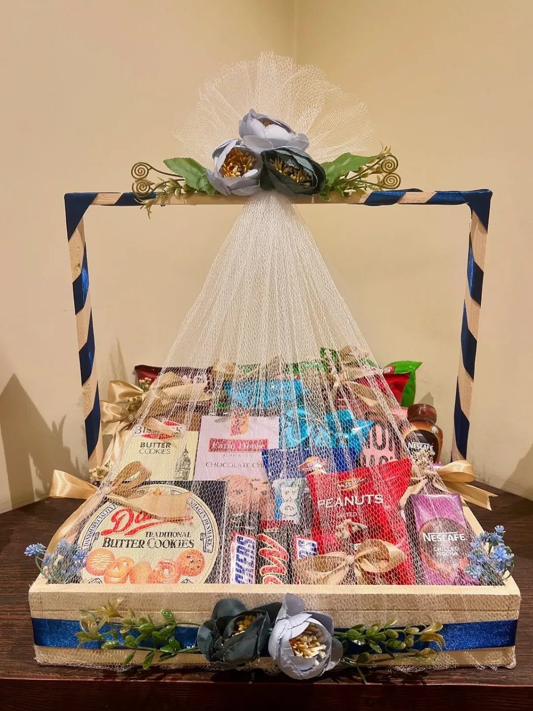 Gift basket filled with cookies, peanuts, and chocolates decorated with blue and gold ribbons.
