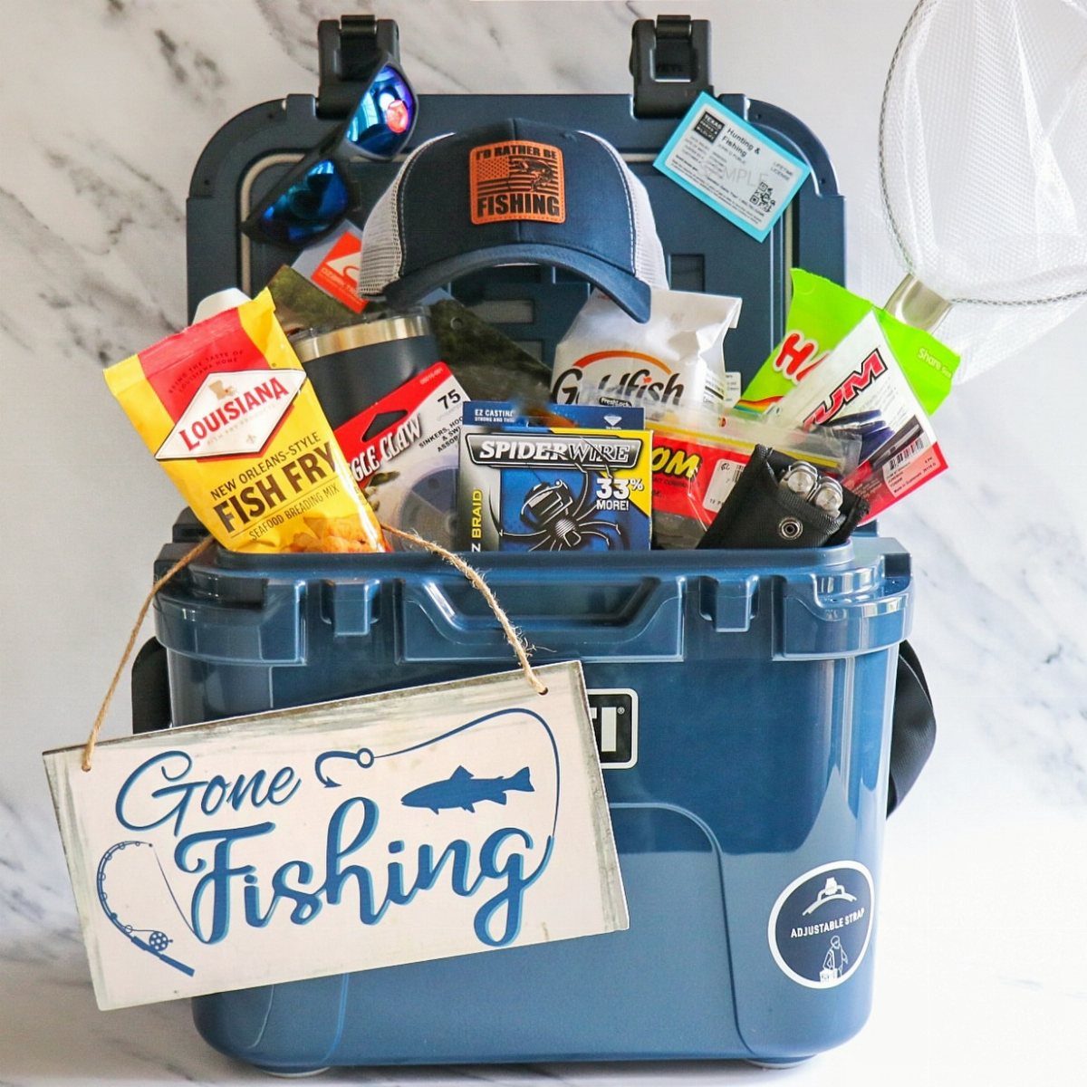 Blue cooler gift basket filled with fishing lures, a cap, and fishing gear.