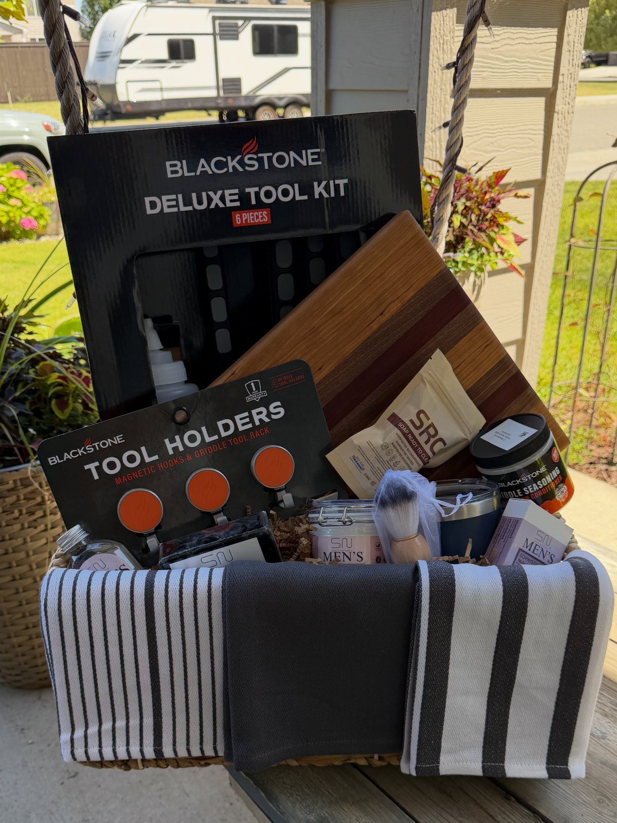 BBQ tool gift basket with Blackstone kit, wooden board, and gourmet food items.
