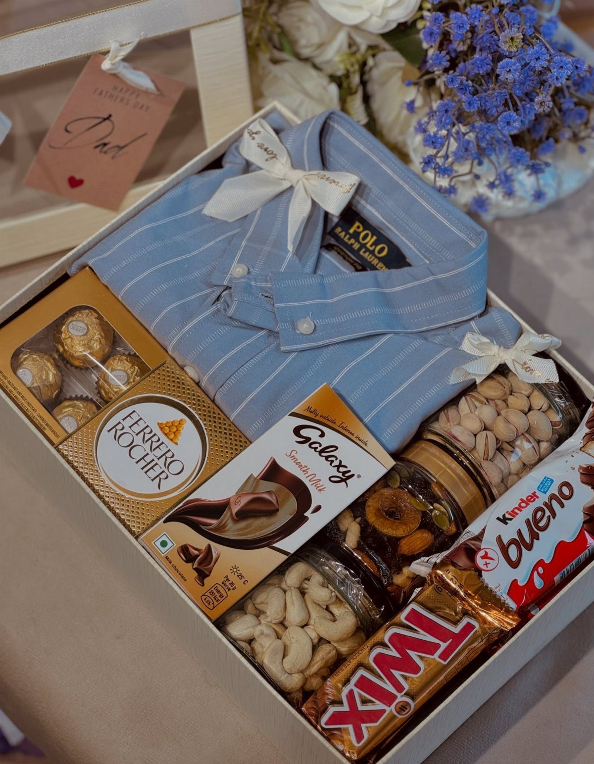Gift box with blue striped shirt, assorted chocolates, and jars of nuts for Father's Day.