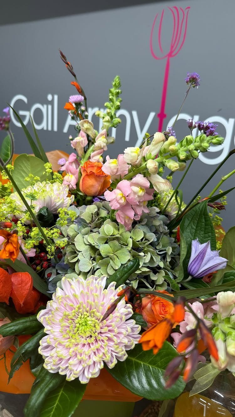 Colorful floral arrangement with pink, orange, and purple flowers and green leaves.