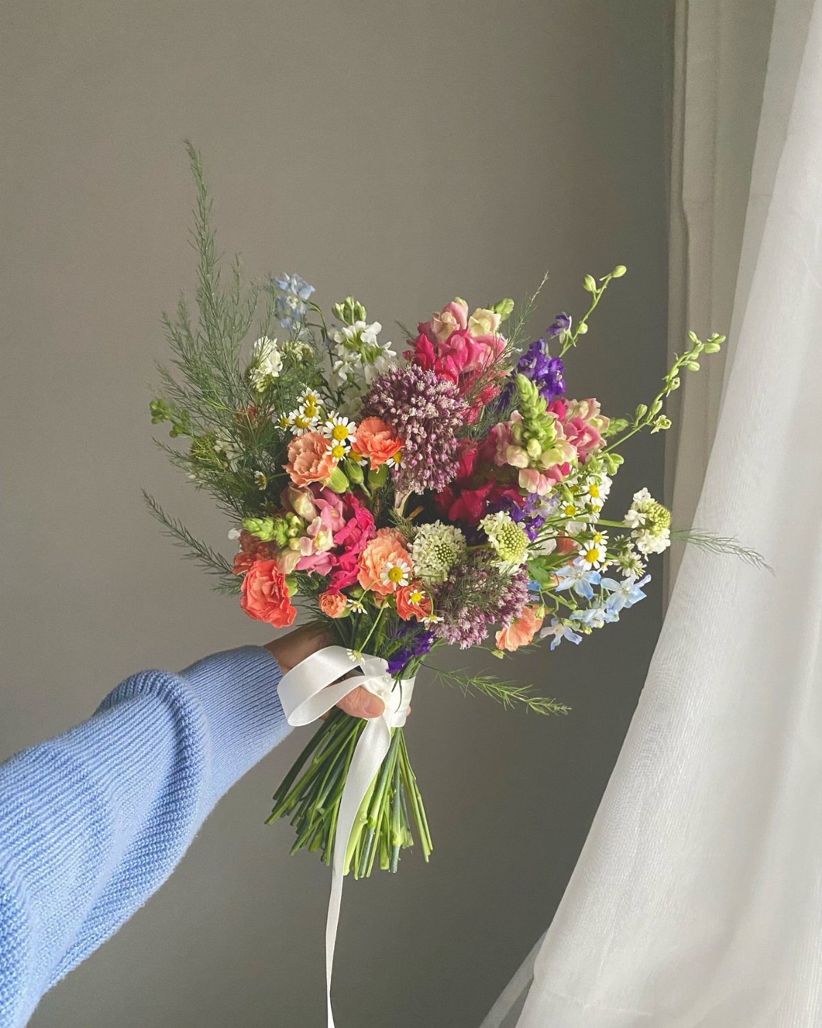 Colorful wildflower bouquet tied with a white ribbon held by a person