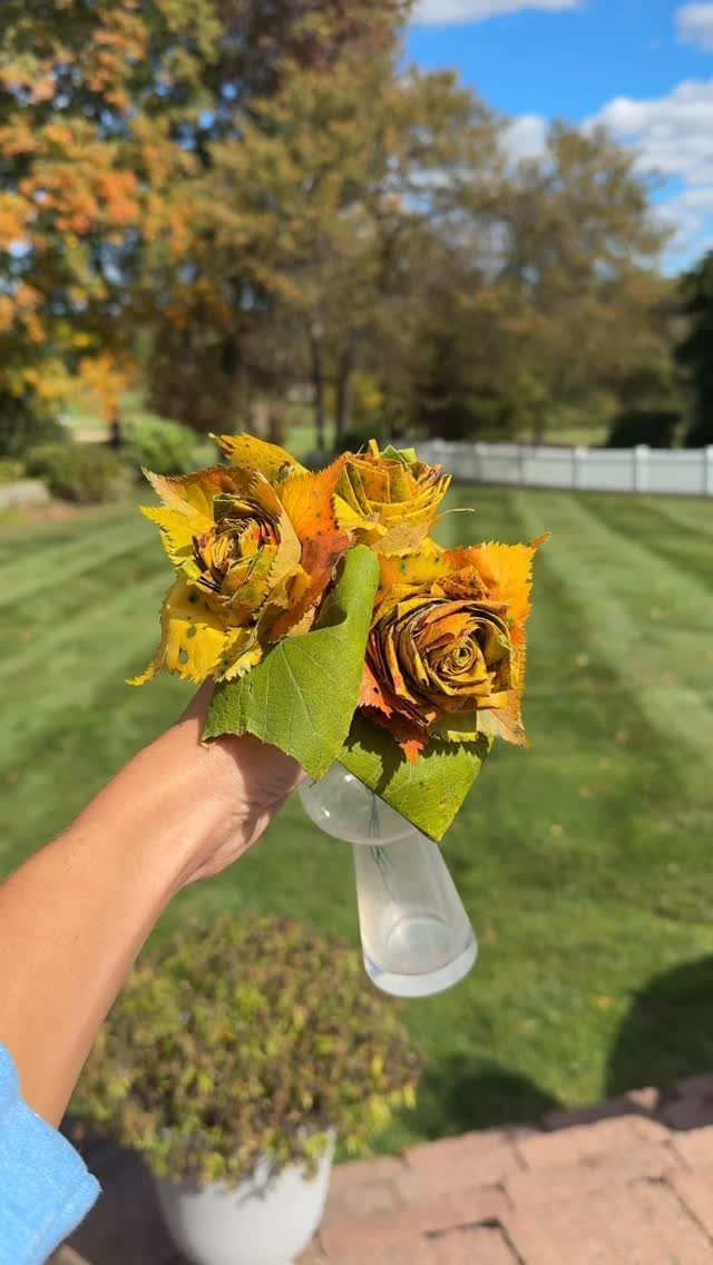 Yellow and orange roses in a small glass vase held against autumn trees.