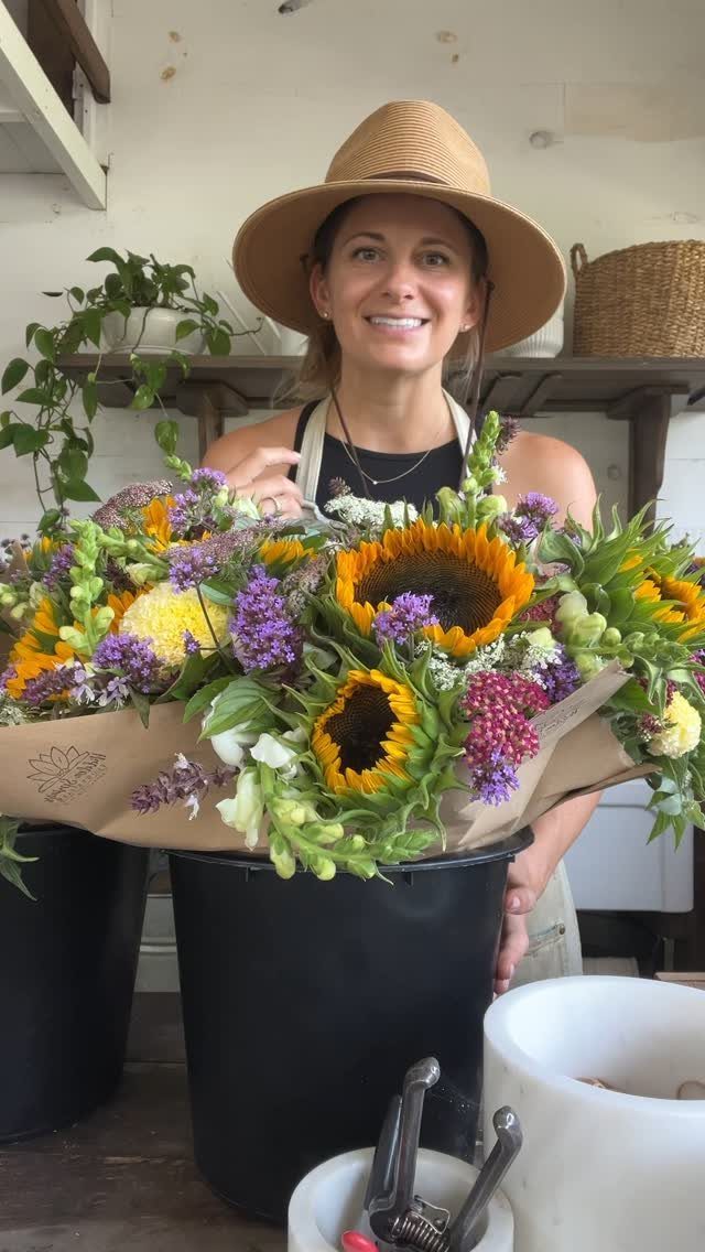 Woman in straw hat holding a large colorful flower bouquet in a bucket.