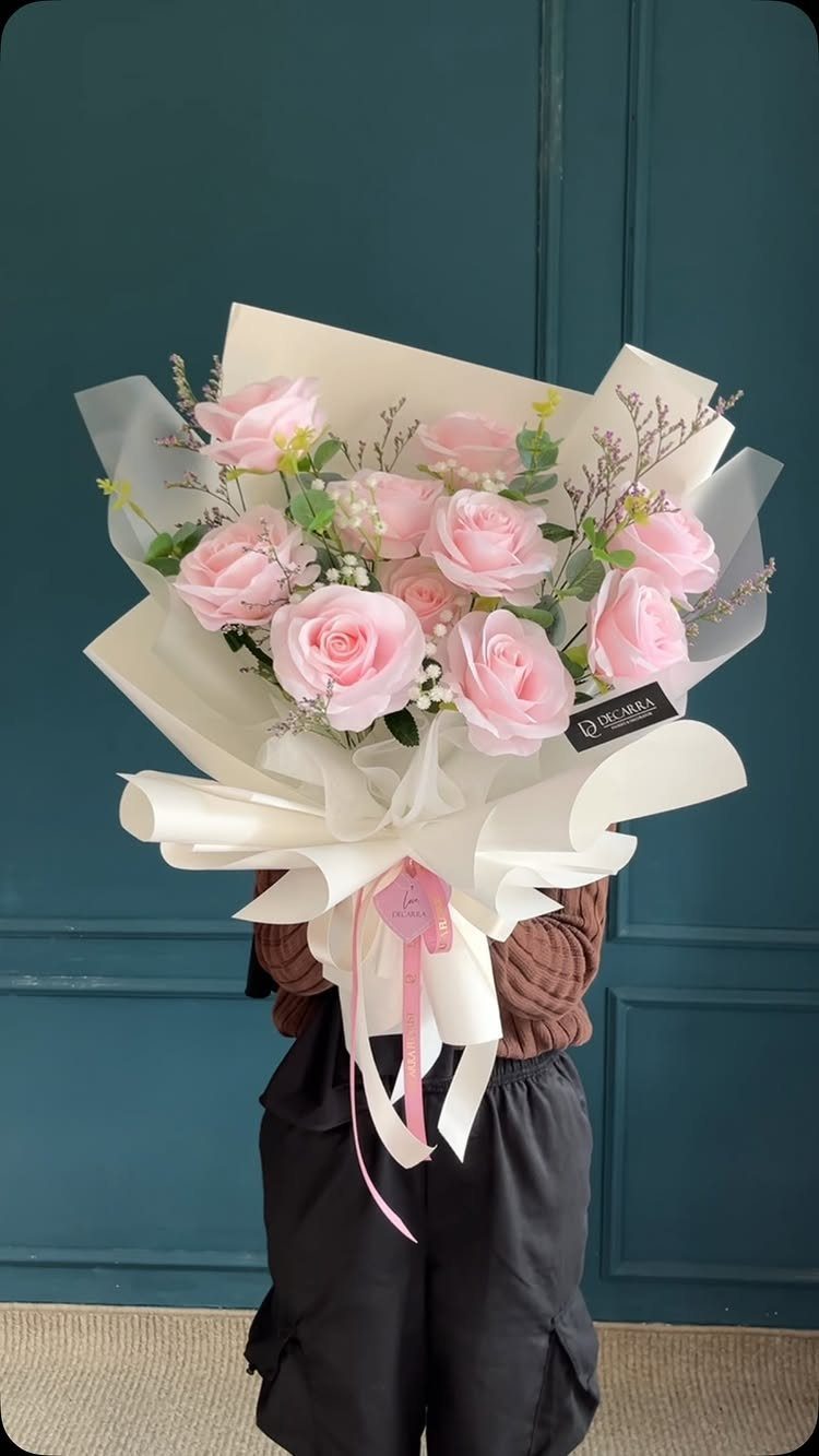 Pink rose bouquet wrapped in white paper and tied with a pink ribbon.