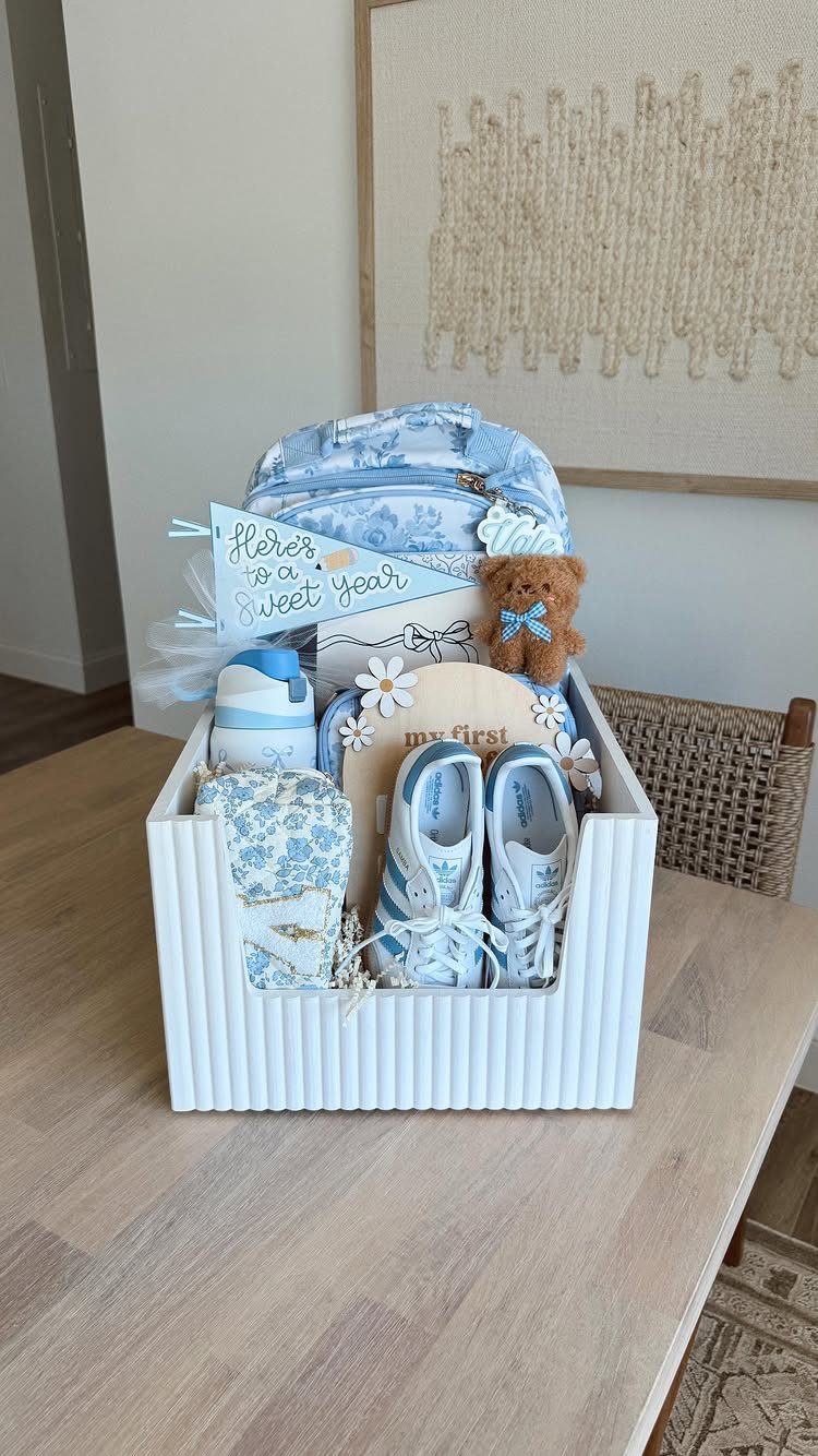 White wooden gift crate filled with blue baby shoes, teddy bear, and blanket.