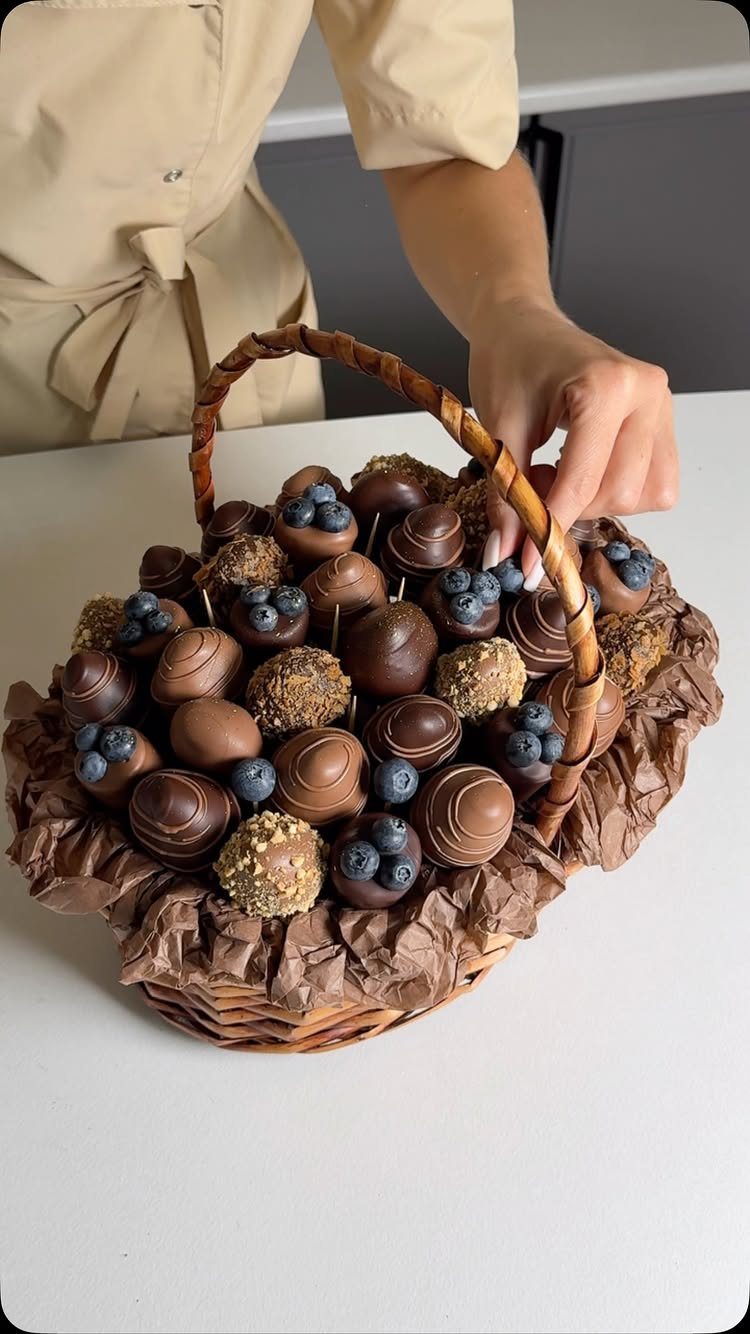 Wicker basket filled with assorted chocolate truffles and blueberries on a white table.