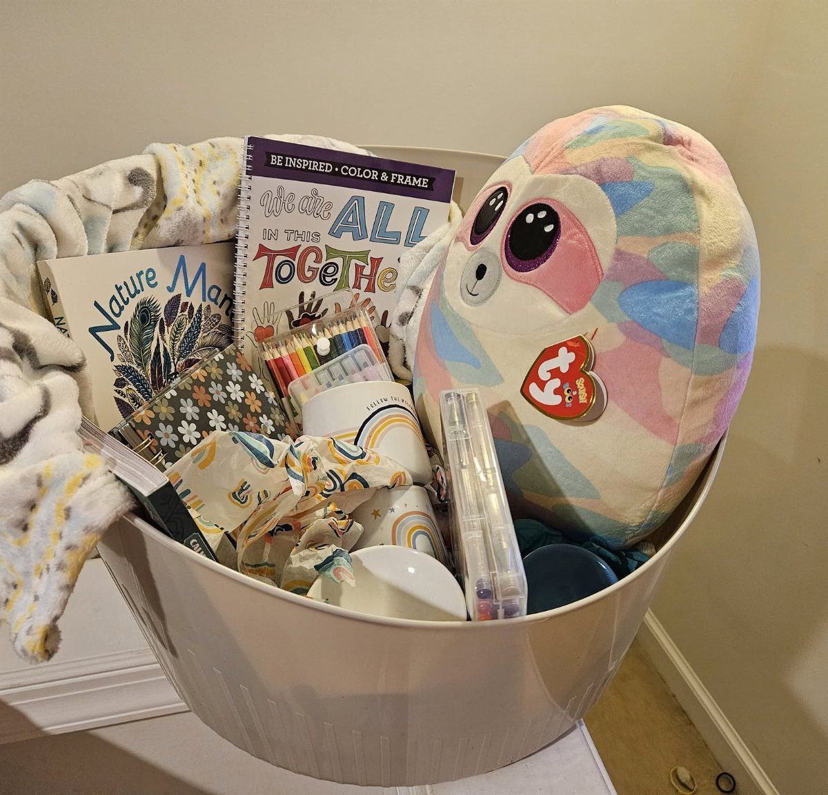 Gift basket containing a plush sloth, coloring book, pencils, and a cozy blanket.