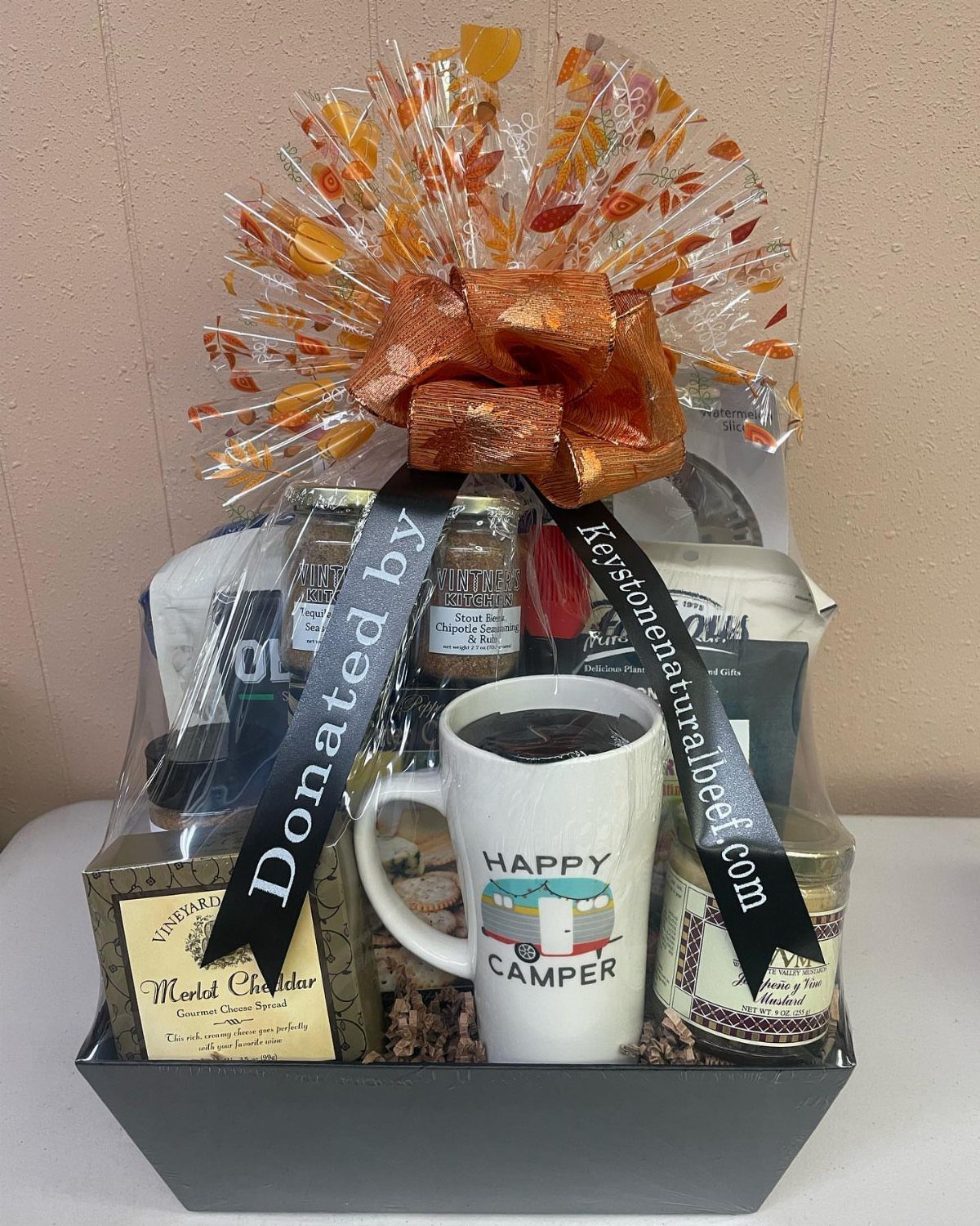 Gift basket with a Happy Camper mug, cheese, and jars wrapped in cellophane.
