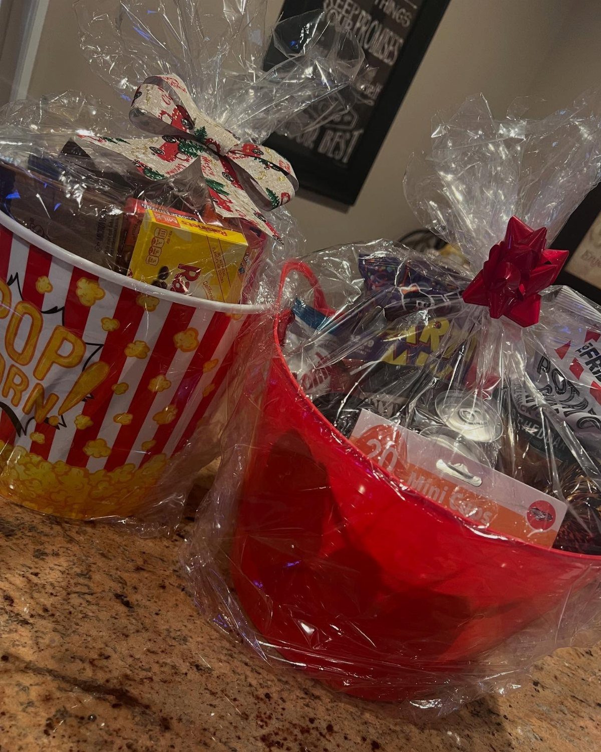 Two wrapped gift baskets, one popcorn-themed and one red, filled with assorted snacks.