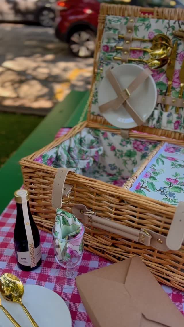 Woven wicker picnic basket with floral lining and gold cutlery on checkered tablecloth