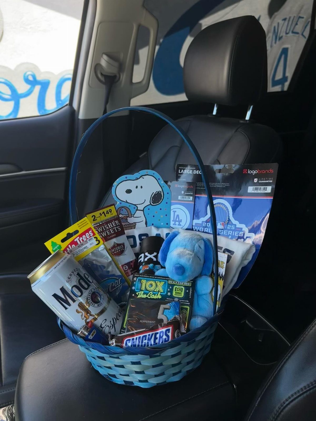 Blue woven gift basket filled with snacks, beer, and sports merchandise on car seat