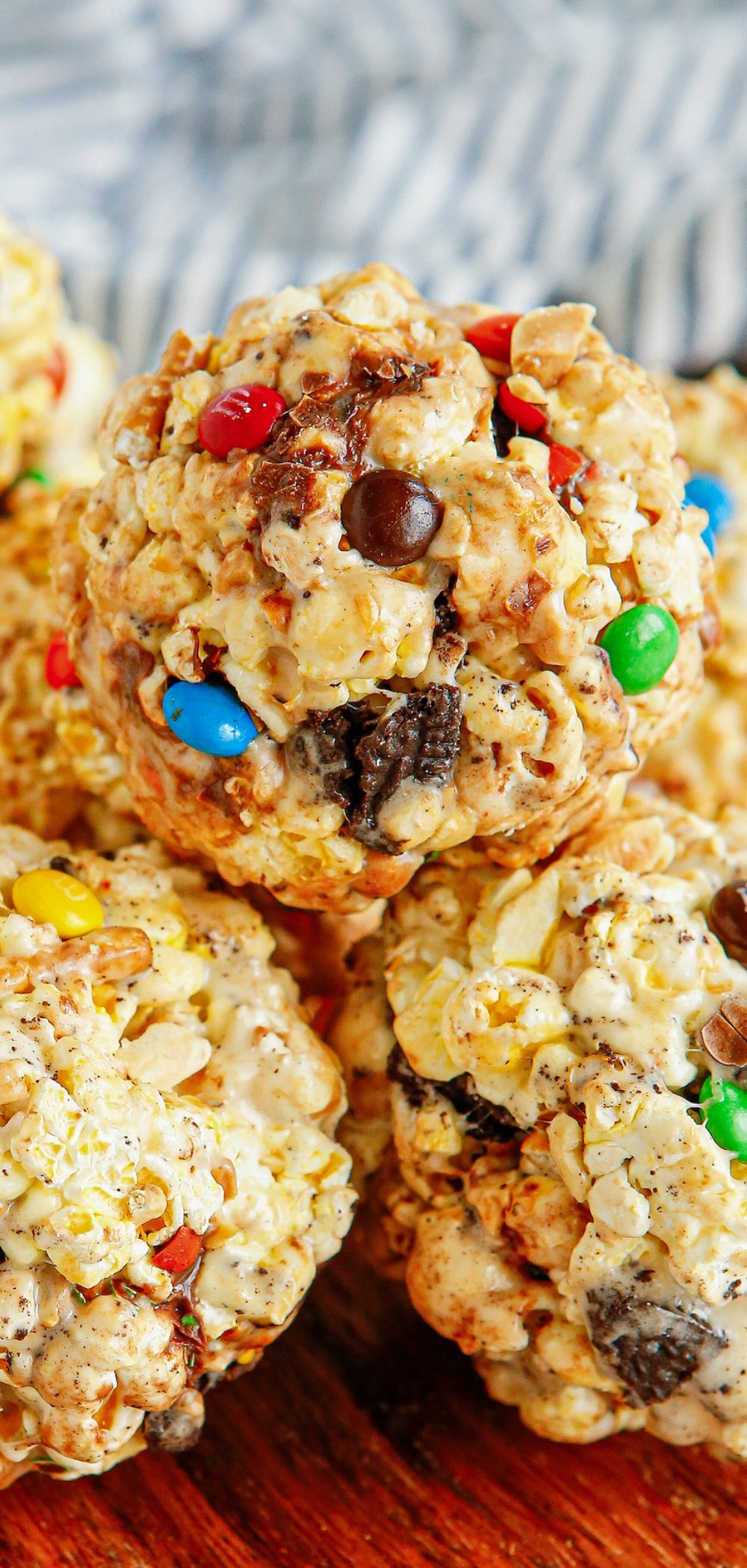Popcorn balls mixed with colorful candy and chocolate cookies on a wooden surface.