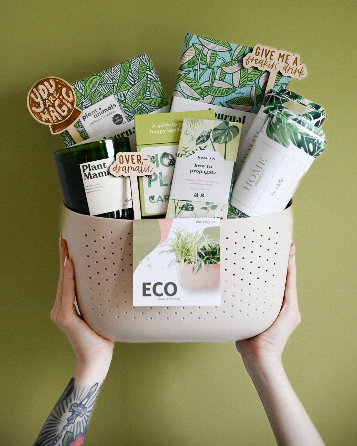 Beige perforated basket filled with plant-themed books, notebooks, and a green candle.