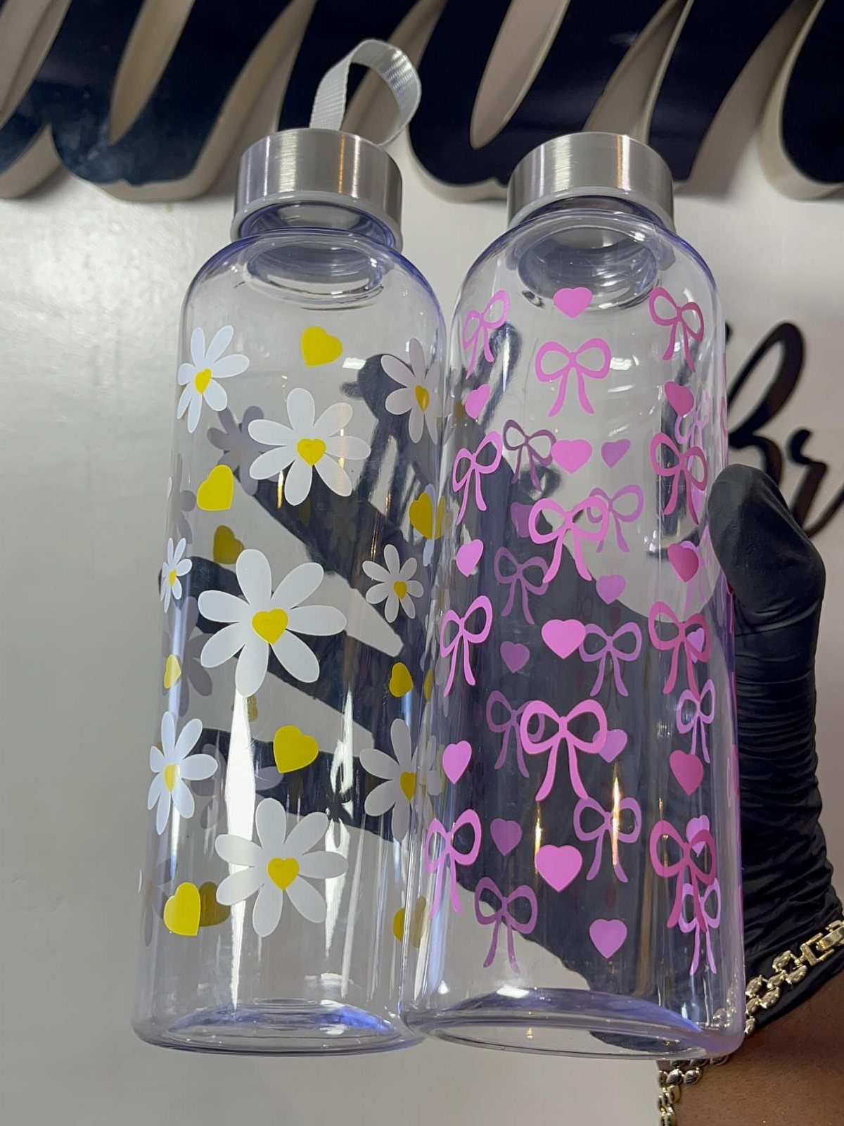 Two clear plastic water bottles decorated with floral and heart patterns and silver lids.