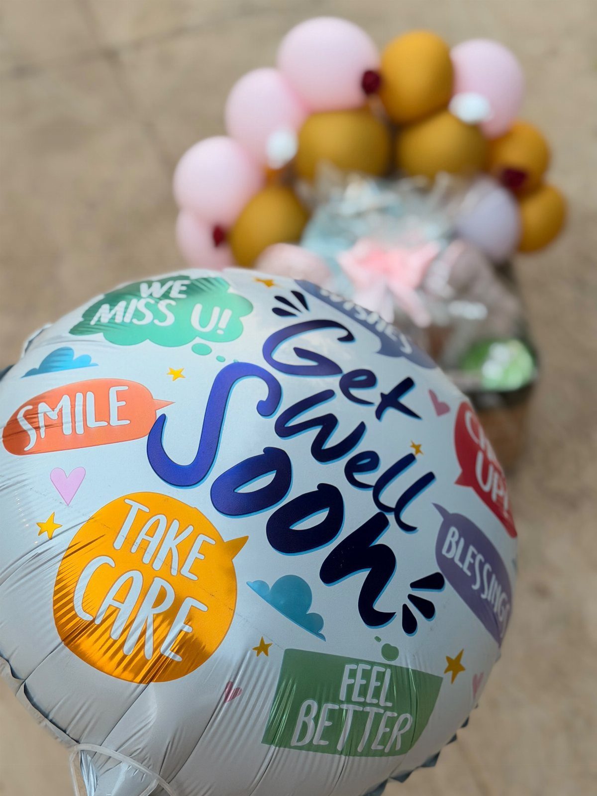 Silver get well soon balloon with colorful text and blurred balloon bouquet background