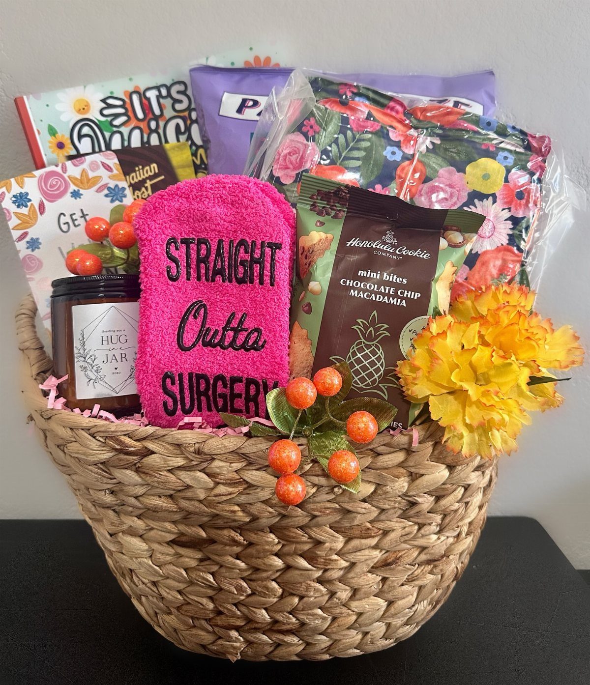 Woven gift basket containing a pink surgery recovery towel, snacks, and yellow flowers.