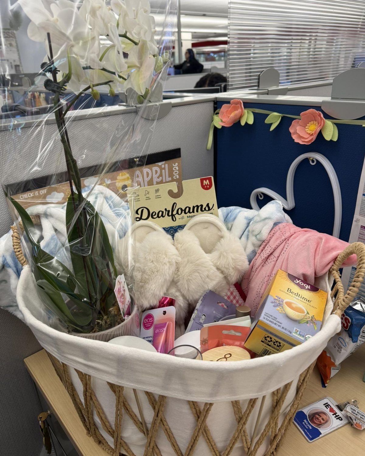 White woven gift basket with orchid, slippers, and tea wrapped in clear cellophane.