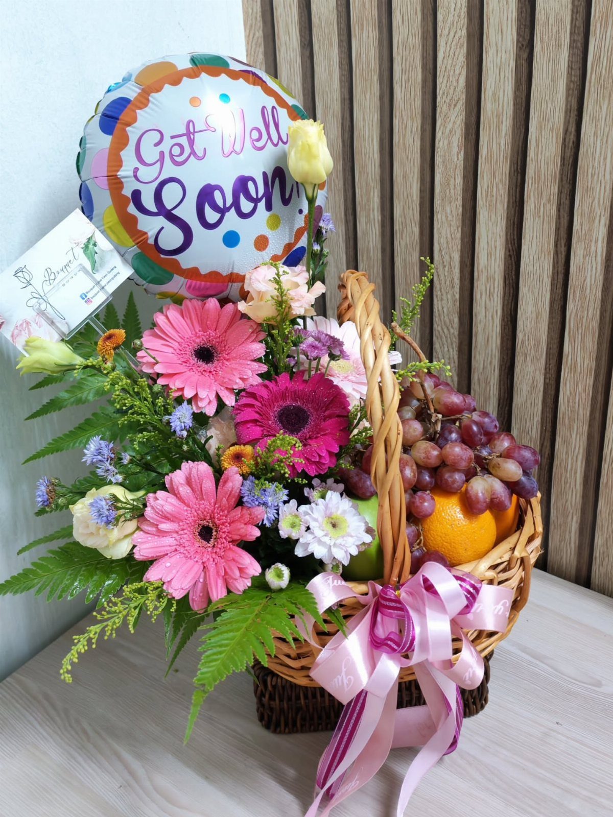 Get well soon gift basket with pink flowers, fresh fruit, and a balloon