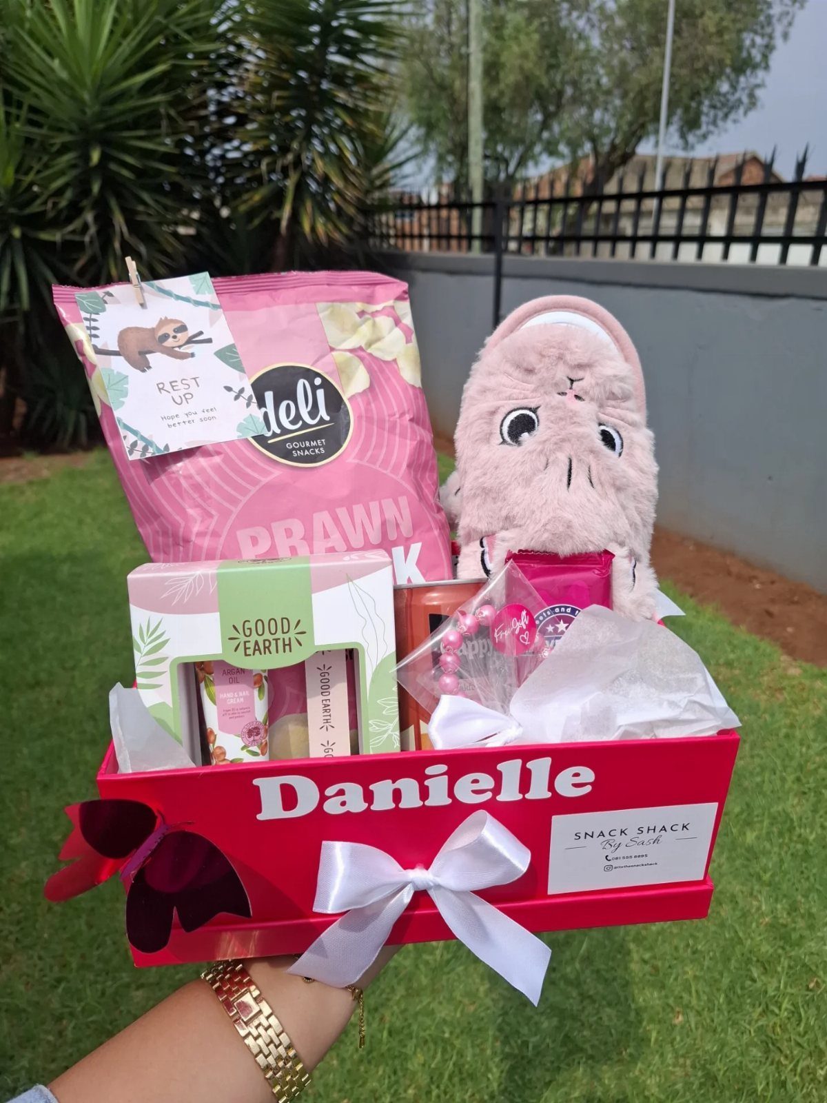 Red gift box with snacks, pink fluffy slippers, and a gift set.