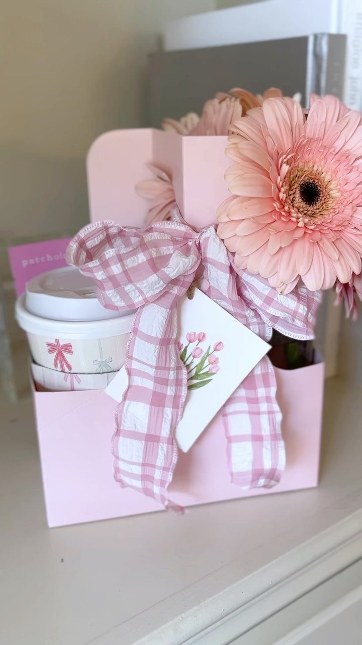 Pink gift box with a travel mug, pink flower, and checkered ribbon.
