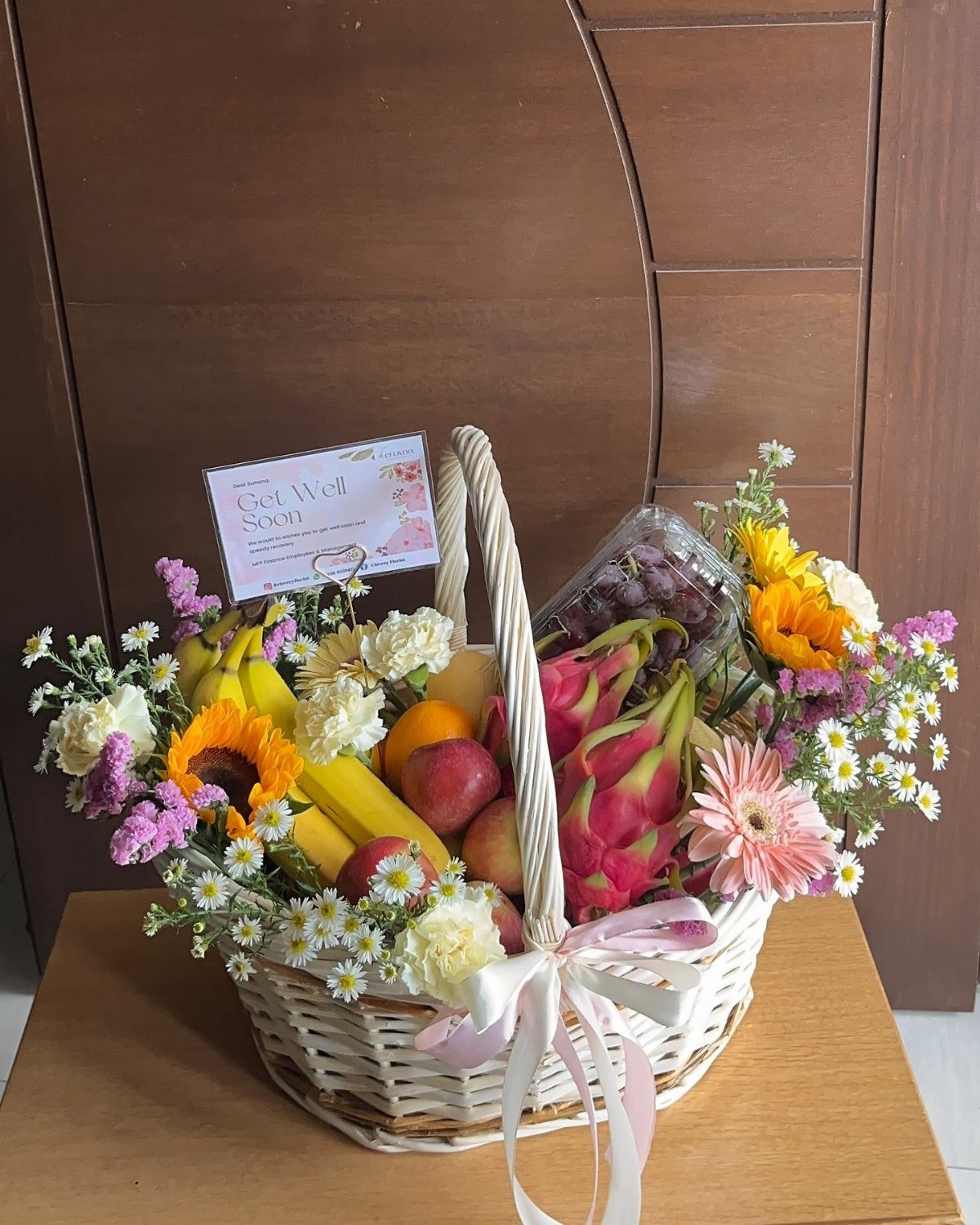 Fresh fruit basket with bananas, apples, and dragon fruit surrounded by colorful flowers.