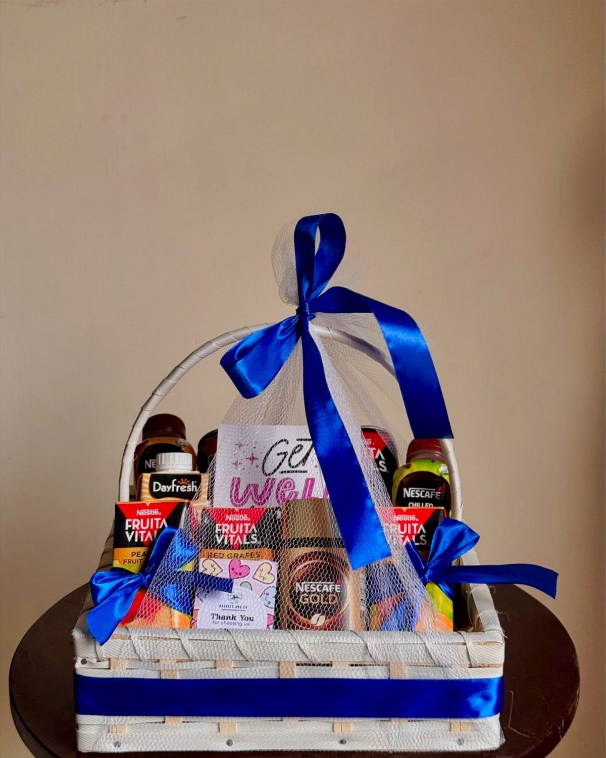 White wicker gift basket with snacks, coffee, and blue ribbons for get well wishes.