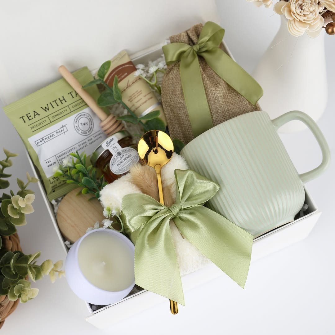 Gift box with green mug, honey jar, tea, and a white candle.